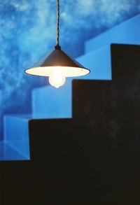 Low angle view of illuminated light bulb hanging against sky