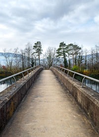 Empty footbridge along plants and trees against sky