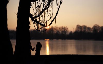 Silhouette man standing by lake against sky during sunset