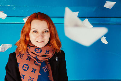 Smiling woman with paper boats hanging against blue wall