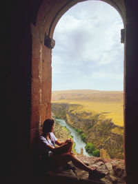 Rear view of woman sitting on window looking at view