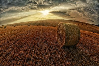 Hay bales on field against sky during sunset