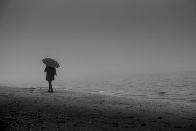 Rear view of woman standing on beach against sky