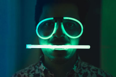 Close-up portrait of man with illuminated neon lights in darkroom