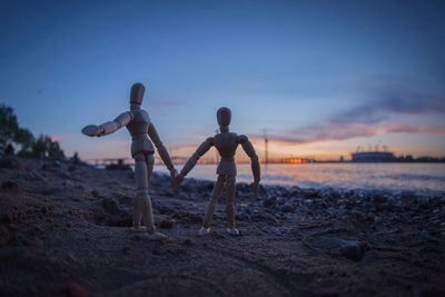 Close-up of wooden figurines on beach against sky during sunset