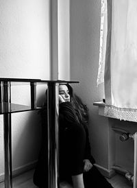 Thoughtful woman sitting by wall at home