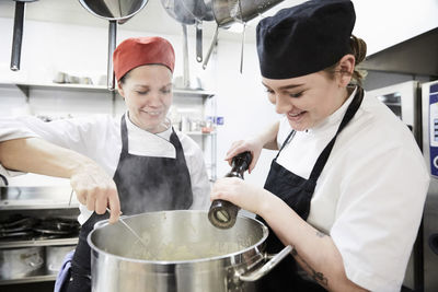 Teacher with female student adding pepper into cooking pan at commercial kitchen