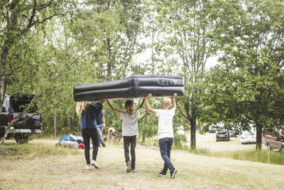 Children carrying inflatable mattress while walking towards car at camping site