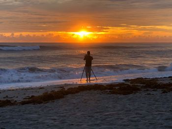 Man photographing at beach during sunset