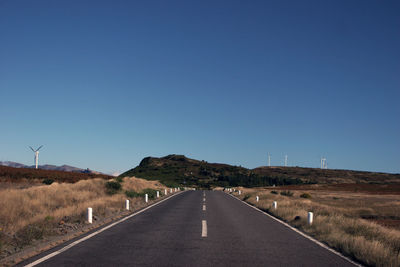 Road leading towards mountains against clear blue sky