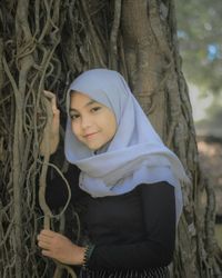 Portrait of smiling woman standing by tree trunk