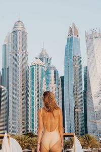 Rear view of woman wearing swimwear standing against modern buildings in city
