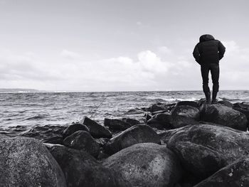 Rear view of man standing on rocks against sea at beach