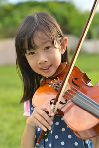 Portrait of girl playing violin on grassy field at public park