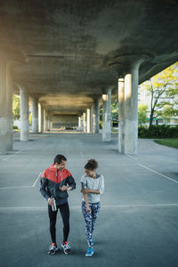 Happy friends walking on street under bridge