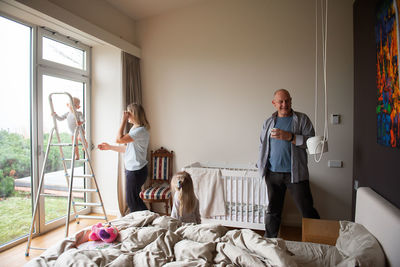 Woman looking at baby boy standing on ladder in bedroom at home