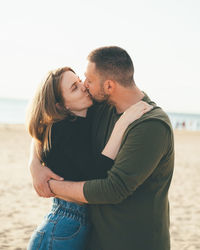 Midsection of couple standing at beach against sky