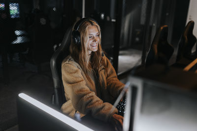 Smiling woman playing video game in illuminated gaming center