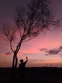 Silhouette man standing by bare tree against sky during sunset