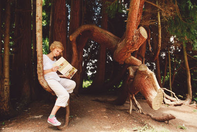 Woman reading book against trees