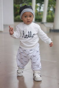 Cute and adorable toddler with a cute smile while standing on the floor in a sporty white costume