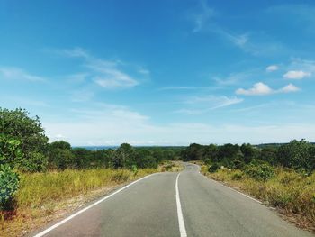 Empty road along plants and trees against sky