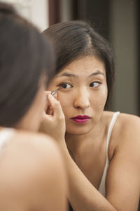 Beautiful woman applies eyeliner while looking in the mirror