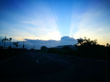 Road by trees against sky during sunset