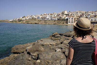 Rear view of woman standing by sea against clear sky