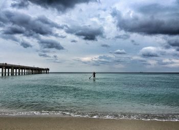 Man paddleboarding on sea against cloudy sky