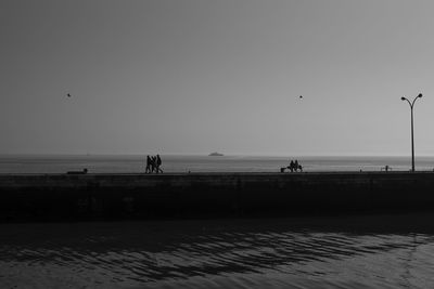 Silhouette people on beach against clear sky