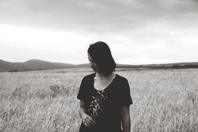 Young woman standing on field against sky