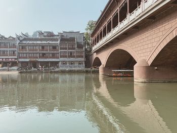 Arch bridge over river by buildings against sky