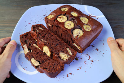 Man's hand holding a plate of fresh baked dark chocolate banana cake placing on the table