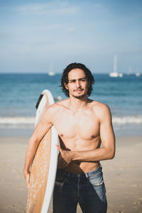 Portrait of young man standing at beach against sky