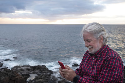 Man using mobile phone at beach against sky