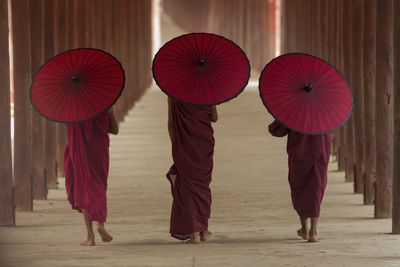 Rear view of monks walking with umbrella in colonnade