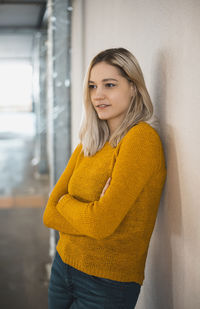 Thoughtful woman with arms crossed leaning on wall