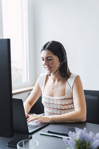 Smiling customer service representative with headset using laptop in office