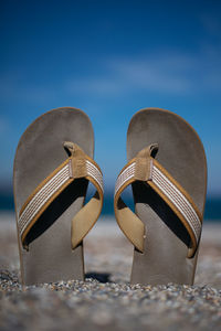 Close-up of sandals at beach against blue sky