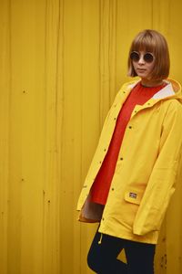 Portrait of smiling young woman standing against yellow wall