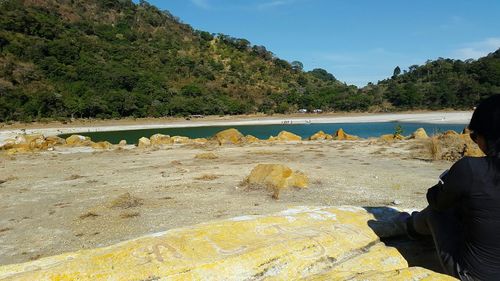 Man sitting on rock by trees against sky