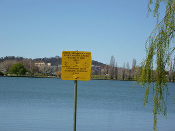 Information sign by lake against clear blue sky