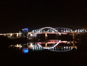 Reflection of illuminated bridge in city against clear sky at night