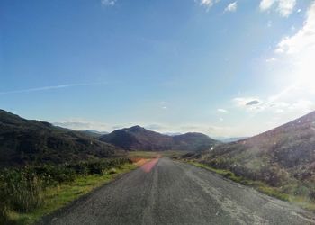 Road passing through mountains against blue sky