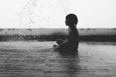 Side view of boy spraying water with hose while sitting outdoors