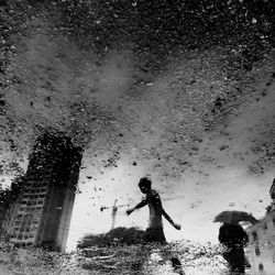 People and building reflecting in puddle on street during rainy season