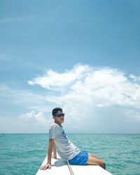 Man sitting on surfboard in sea against blue sky