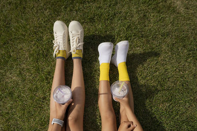 Girls wearing white shoes holding milkshakes on grass at park