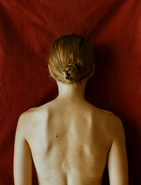 Rear view of shirtless young woman standing against red wall. uncertainty, love, mental health